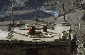 20066514 NEPAL Annapurna Mountains Architecture Woman spreading grain out to dry on roof of rural building.