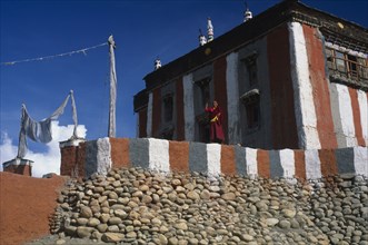 NEPAL, Mustang, Tsarang, Head monk looking out from terrace of temple painted with coloured stripes