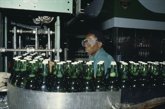 NIGERIA, Industry, Brewery with man wearing safety goggles working  behind machinery and green
