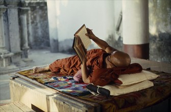 MYANMAR, Yangon, Buddhist monk lying on raised platform and reading in Shwedagon Pagoda.