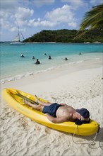WEST INDIES, St Vincent & The Grenadines, Tobago Cays, Man lying in kayak sunbathing on the beach