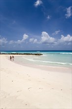 WEST INDIES, Barbados, Christ Church, Couple walking towards sea defences on Rockley Beach also