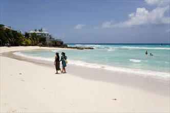 WEST INDIES, Barbados, Christ Church, Two women walking on the sand past a couple in the sea at