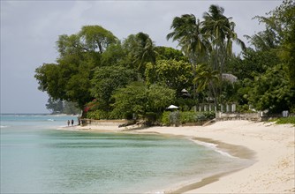WEST INDIES, Barbados, St Peter, People walking along beach at Gibbes Bay past one of the exclusive