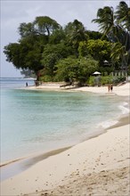 WEST INDIES, Barbados, St Peter, People walking along beach at Gibbes Bay past one of the exclusive