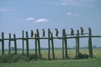 MYANMAR, People, Line of monks with fans crossing wooden bridge raised high above agricultural land