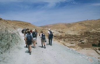 MOROCCO, High Atlas Valley, Tourist group following man on horseback along steep stony mountain