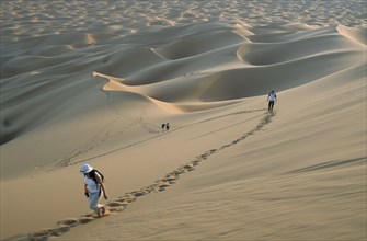 MOROCCO, Sahara, Merzouga, Tourists walking through desert landscape leaving trails of footprints