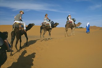 MOROCCO, Sahara, Merzouga, Guide leading tourist camel train through desert landscape.