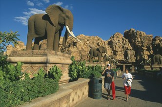 SOUTH AFRICA, North West, Sun City, Tourist visitors on avenue lined with statues of elephants.