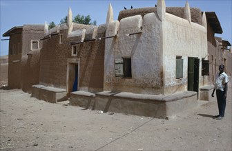 NIGERIA, Kano, Traditional Hausa dwelling and mud architecture with man standing outside.