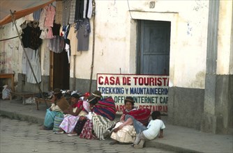 BOLIVIA, North, Sorata, Indigenous women and children sat on pavement outside trekkers agency