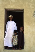 OMAN, Sur, Sheikh of Al-Ghalila with his two children in the doorway to his house.
