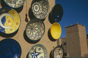 MOROCCO, Ouarzazate, Painted ceramic dishes displayed on wall with Kasbah Taorirt partly seen