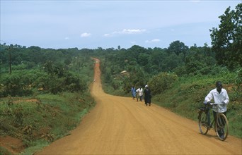 UGANDA, Road, Murram dirt road stretching into distance with cyclist approaching.