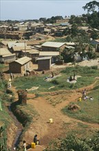 UGANDA, Kampala, Looking across the poorer town outskirts. Women collecting water in foreground.