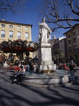 FRANCE, Aix en Provence, "Statue in centre of water fountain, people sat on edge. Carousel and
