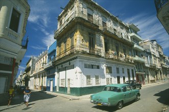 CUBA, Havana, Street corner with traditional buildings with overhanging balconies.  Turquoise car