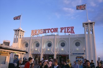 ENGLAND, East Sussex, Brighton, Brighton Pier with groups of people in the foreground.