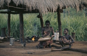 CONGO, Tribal People, Woman and children sitting beneath thatched shelter in village with pot on