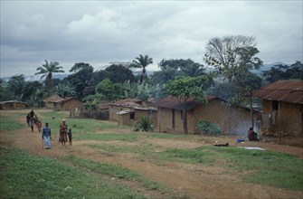 ANGOLA, Vige, Mud brick village houses with people on unmade road outside.