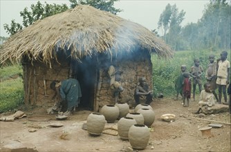 RWANDA, Traditional House, Tutsi potter and family outside thatched mud brick home.