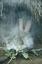 SUDAN, South, Rituals, Azande tribeswoman kneeling over fire to purify herself after giving birth.