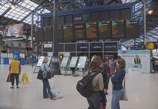 ENGLAND, East Sussex, Brighton, Train station interior with people gathered around departure board.