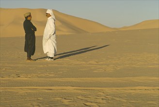 ALGERIA, Desert, Two men standing in the desert in conversation casting strong shadows across the