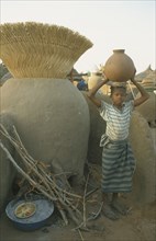 BURKINA  FASO, Bisaland, Sigue Voisin, Near Garango. Young girl carrying water vessel on head.