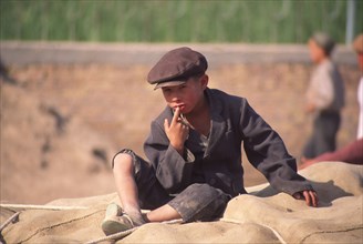 CHINA, Xinjiang Province, Kashgar,  Tajik boy sat on sacks