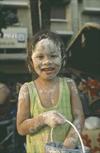 THAILAND, Bangkok, "Young girl with bucket, covered in mud at the Songkhran Festival. Thai New