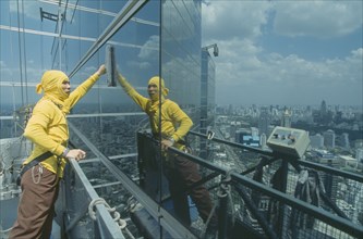 THAILAND, Bangkok, "Man on a lift, cleaning the outside windows of a large building."