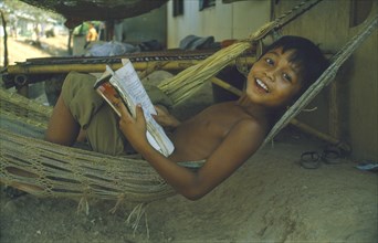 THAILAND, Children, Smiling boy in hammock with open notebook.