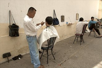 VIETNAM, South, Ho Chi Minh City, Men cutting hair in a hair Salon on the street