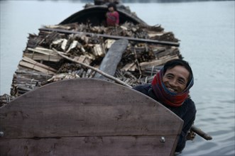 VIETNAM, Central, Hue, Smiling boatman on barge laden with timber.