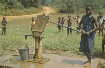 GHANA, Children, Young girl using village hand pump near Euchi.