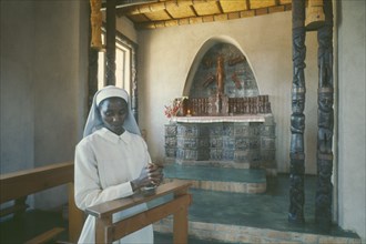 ZIMBABWE, Serrisima Mission, Young nun praying in front of altar inside mission.