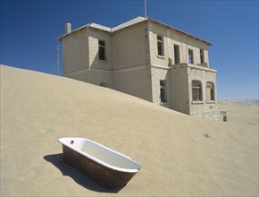 NAMIBIA, Kolmanskop, A house with a bath tub in the foreground  with desert sands encroaching.