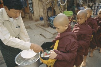 MYANMAR, Mandalay , Giving early morning Alms to young Monks queuing up at side of road.