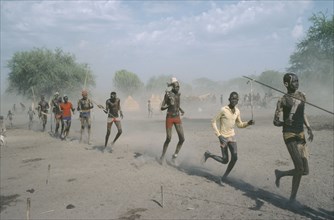 SUDAN, People, Young Dinka men carrying spears and running in line.