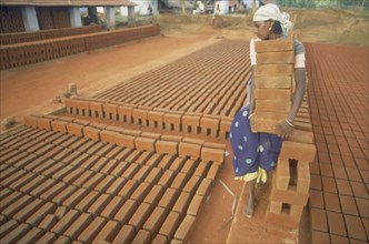 INDIA, Tamil Nadu, Barefooted young woman carrying large stack of bricks at brick works.