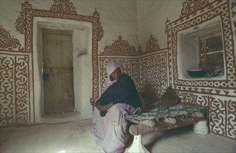 MAURITANIA, Oulata, Woman in interior of traditional mud house with decorative painted design on