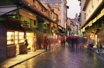 ITALY, Tuscany, Florence, "Street scene at dusk with shop fronts lining Ponte Vecchio, crowds in
