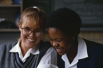 SOUTH AFRICA, Johannesburg, Black and white schoolgirls sharing a joke in the classroom.