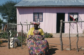 NAMIBIA, Epukiro Reserve, Herero lady in traditional dress sitting outside her home.