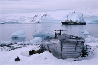 ANTARCTICA, King George Island, Old whale boat on land with Greenpeace ship in distance.