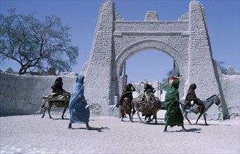 NIGER, Architecture, Town gate with women walking or riding donkeys past below.