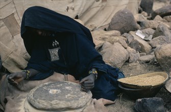 NIGER, People, Women, Tuareg woman grinding flour using two large circular stones for bread making.