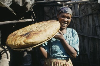 ETHIOPIA, Shoa Province, Nazareth, "Smiling woman holding up large, circular loaf of bread."